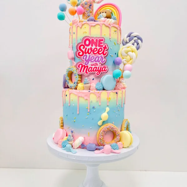 Shop 241 One Sweet Year birthday cake Birmingham — pastel ombré drip cake with mini doughnuts, rainbow topper and sprinkles, handmade by Khalid's Kakes