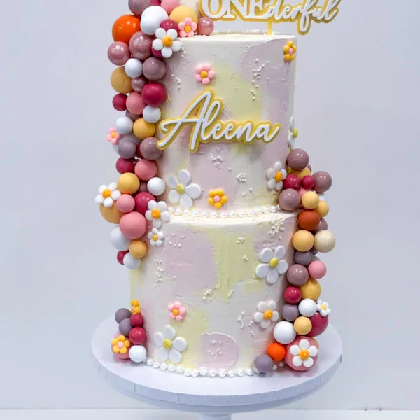 Shop 321 Daisy ONEderful Cake Birmingham — pastel two-tier 1st birthday cake with daisy flowers and a gold topper, handmade by Khalid's Kakes